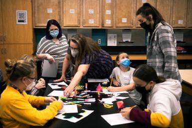 Four middle school girls work on creating paper models of shapes like pyramids, cubes and dodecahedrons with the help of Dr. 玛格丽特·沃茨博士. 芭芭拉·詹宁斯·赫尔佐格, 谁在澳门威尼斯人网址教数学, 和Bailee back, a junior elementary and special education major. They are in one of the classrooms in Doane's Lied science building. 